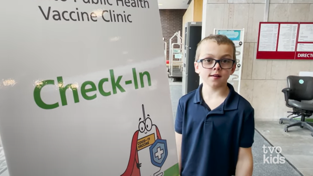 Client ambassador Alex Winter standing next to check-in sign for a vaccine clinic at Holland Bloorview's.