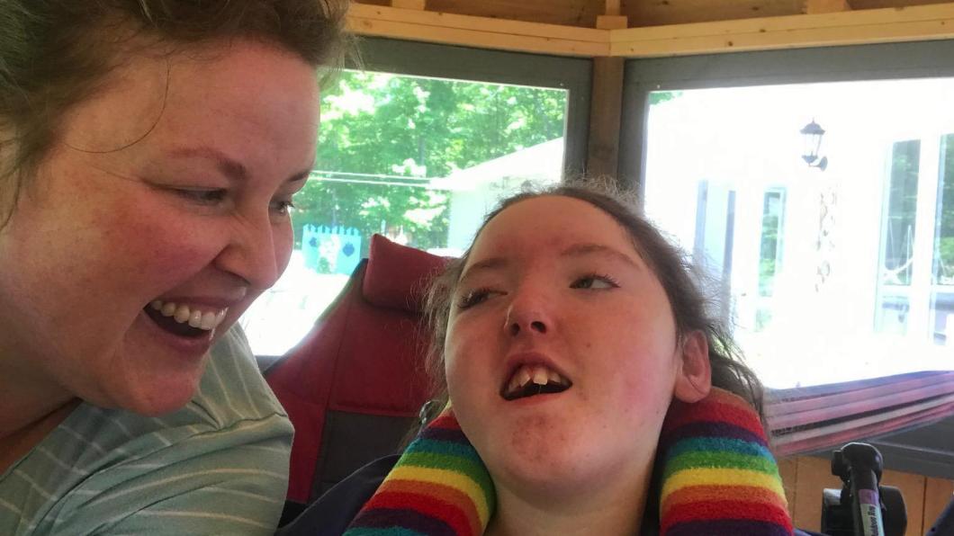 Image of mother and daughter smiling, daughter has a colourful striped neck support