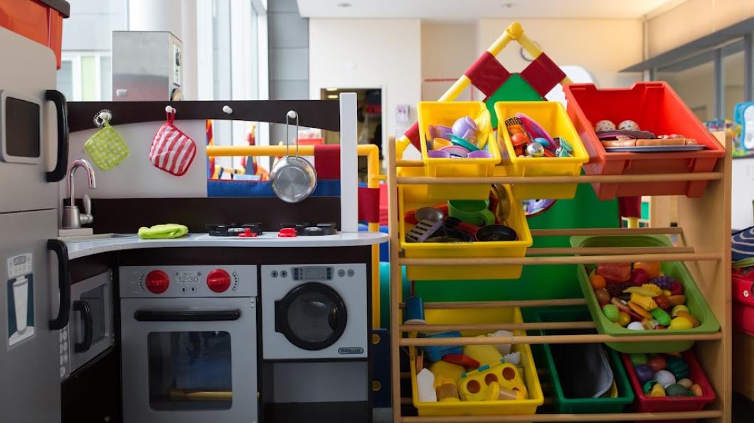 Bins of red and yellow children's toys. The toys are on a shelf next to black-and-white toy kitchen appliances, including a sink, microwave and washing machine.