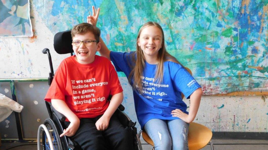 Two kids, one of whom uses a wheelchair, laughing