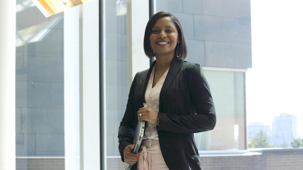 Woman with dark hair and black blazer smiles while holding laptop