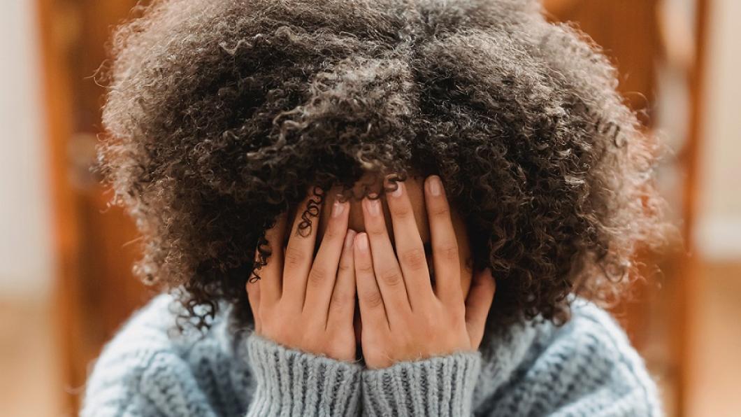 Image of young adult covering their face with their hands, hunched over