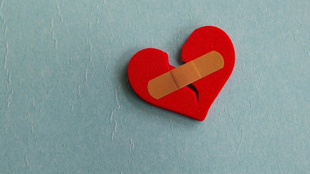 Broken red heart with bandage on blue background