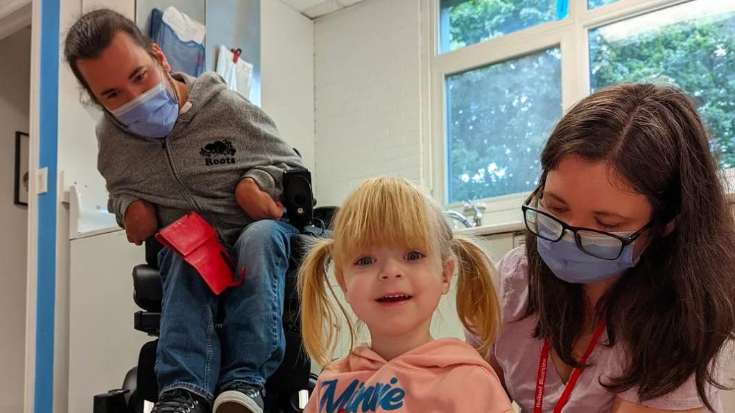 Toddler girl with blonde hair pats black rabbit with mother and dad in a wheelchair