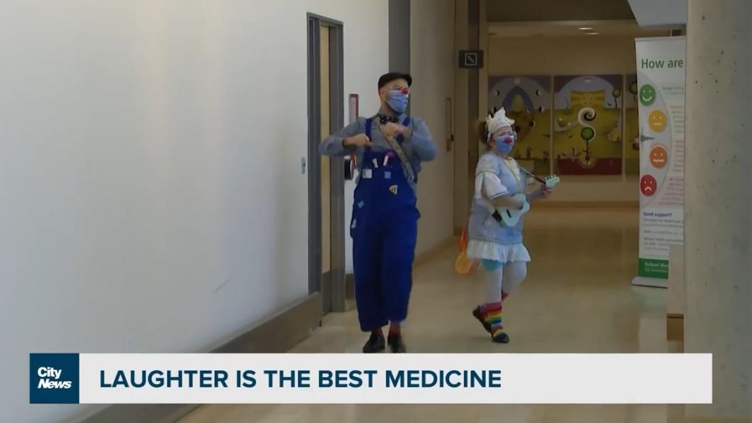 Two of our therapeutic clowns dancing and playing ukulele in a Holland Bloorview hallway