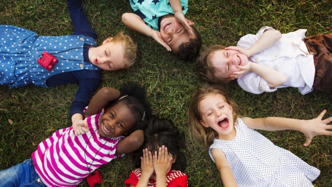 Children lie on grass in circle with different excited expressions on their faces