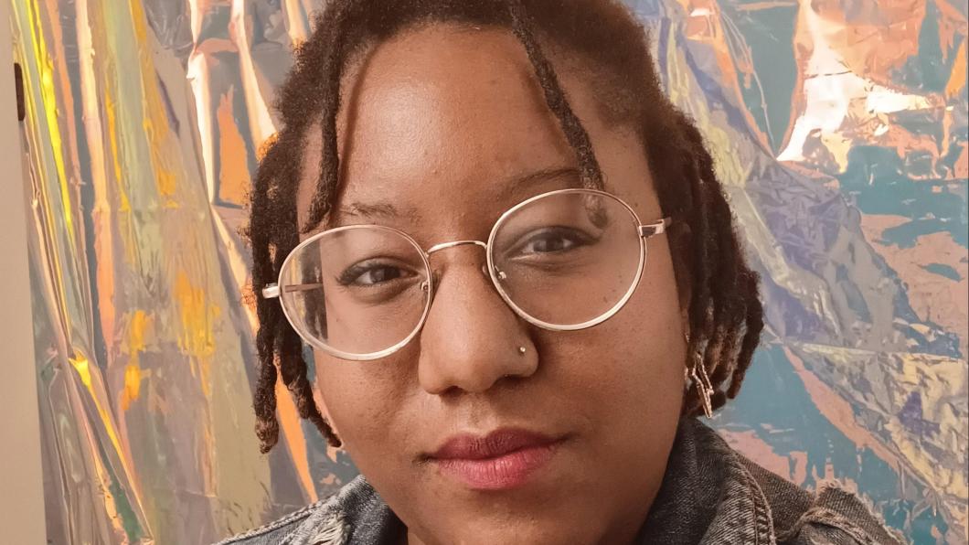 Young woman with glasses and twists in hair against backdrop of abstract painting