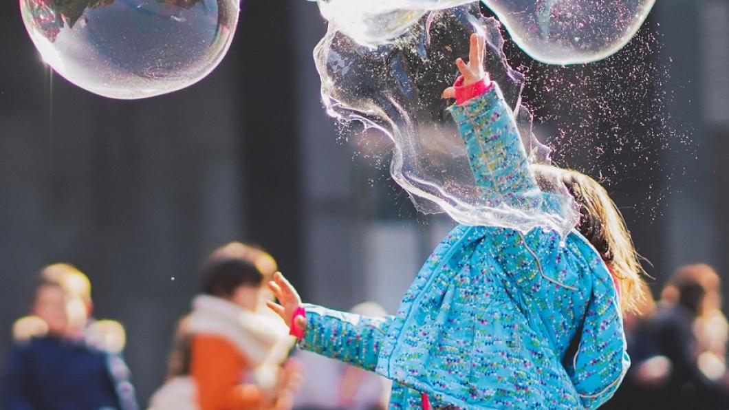 young child wearing blue jacket plays with bubbles 