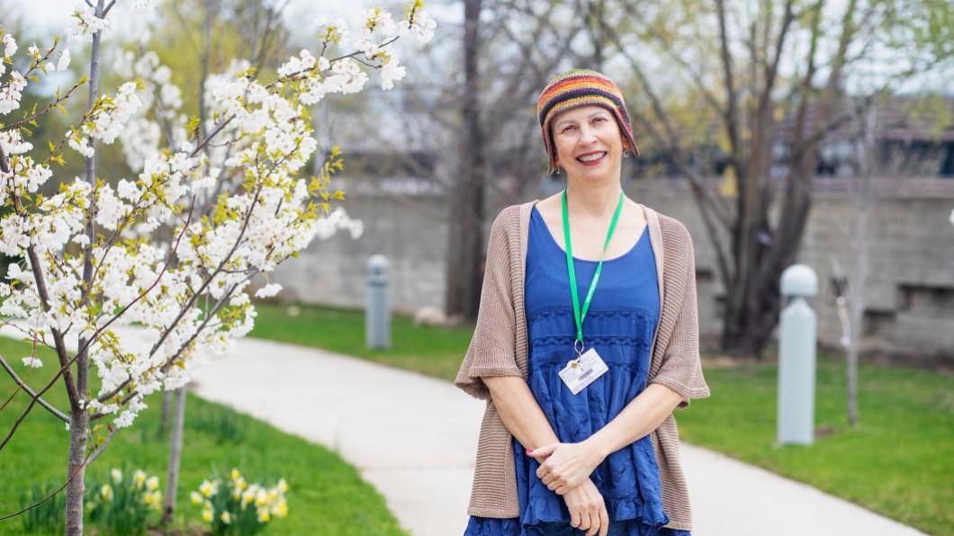 Woman with multicoloured hat stands beside blooming tree.