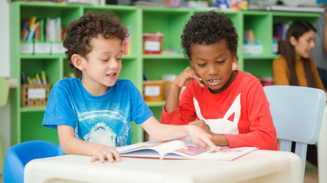 Two boys in bright shirts look at book in classsroom