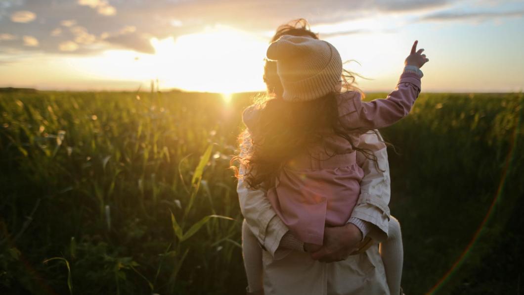 Woman holding girl in field with sun shining