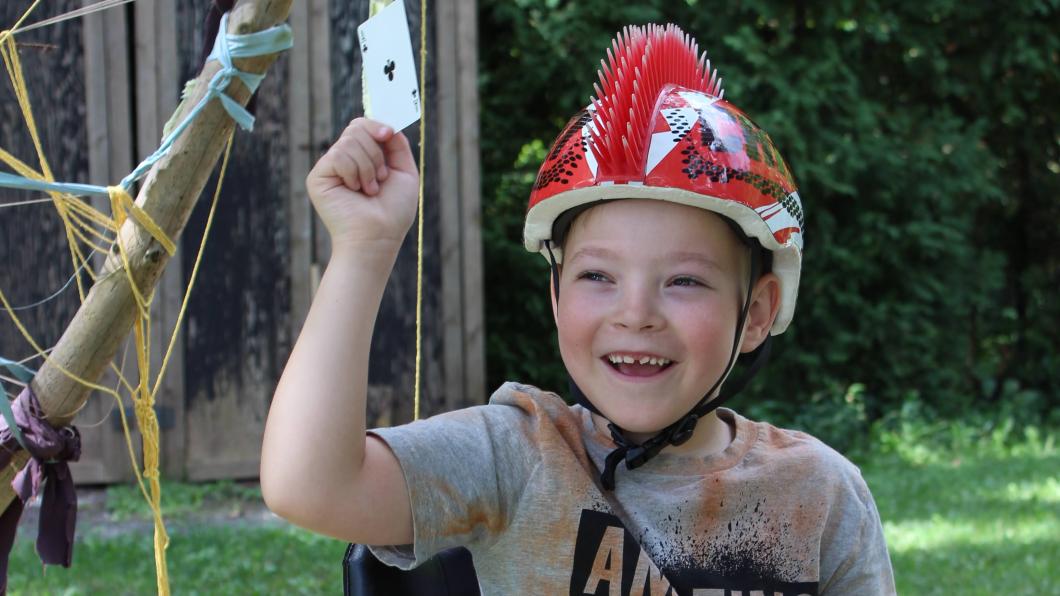 Young boy riding an adaptive bike holding up playing cards. 