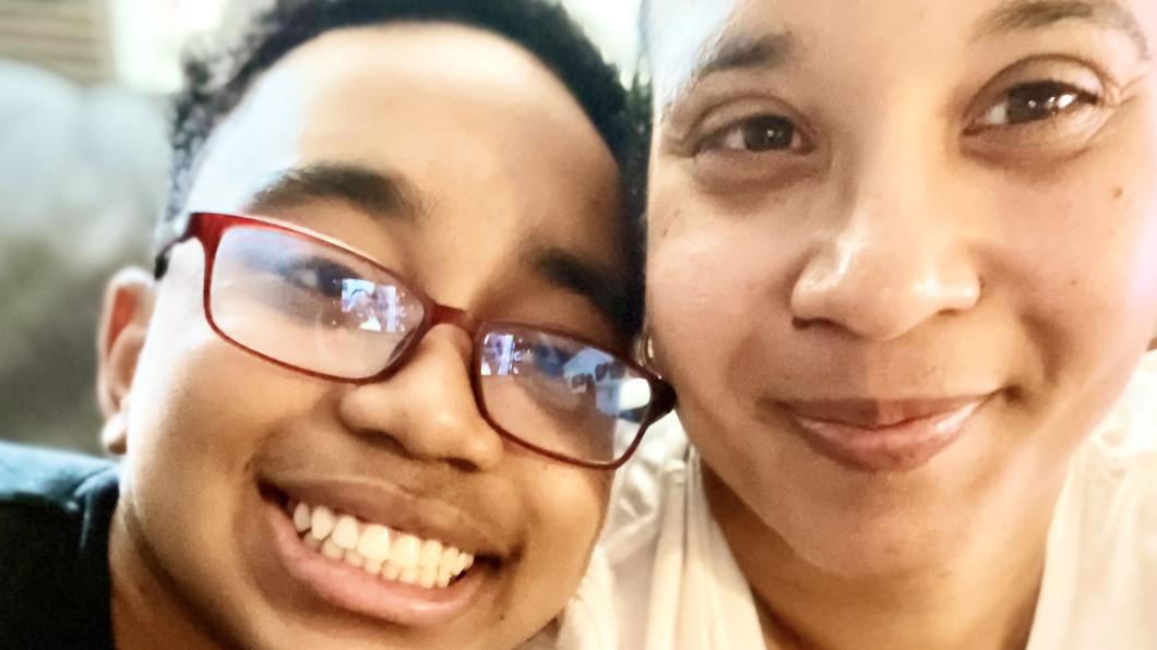 Close up of woman's face smiling beside boy with short curly dark hair and glasses smiling