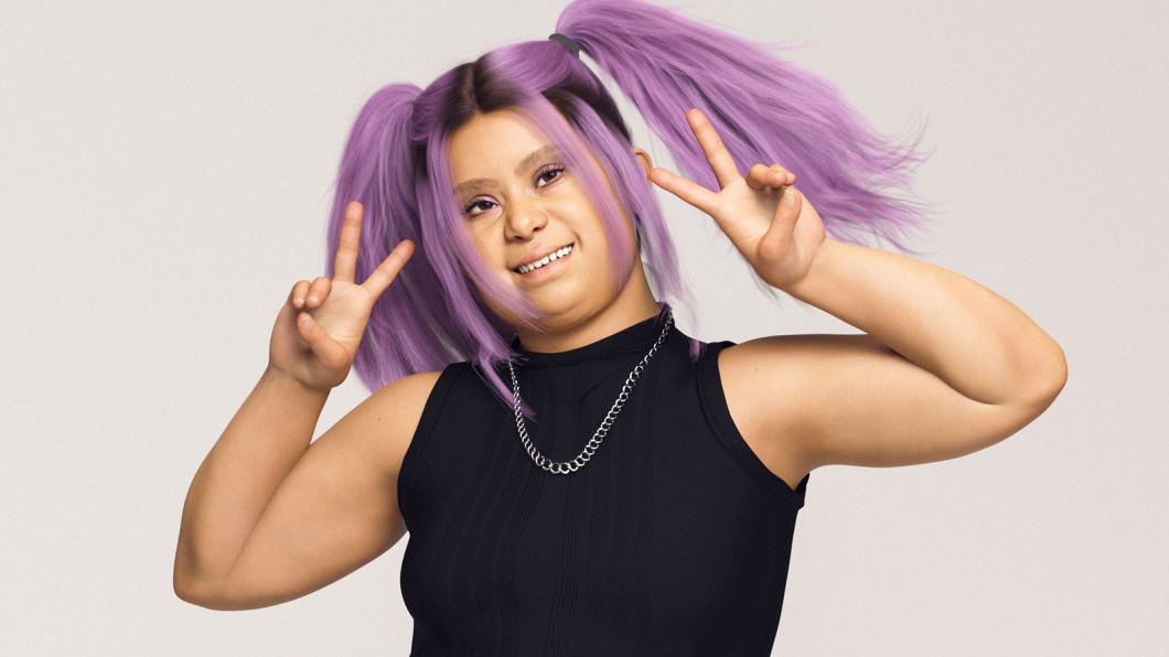 Woman with purple hair and black shirt smiles and holds up two peace signs