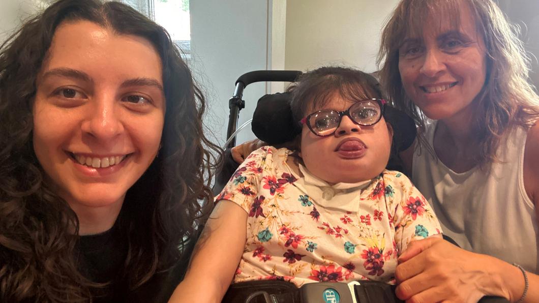 Woman with long dark hair smiles beside woman with glasses in a wheelchair beside woman with long blonde hair