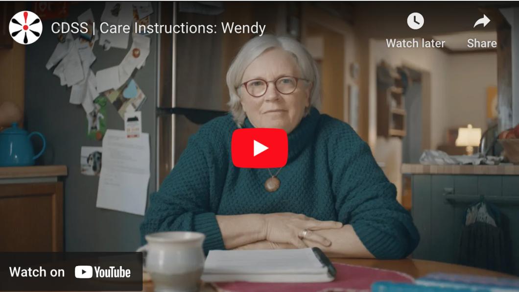 Woman with white hair sits at desk with hands folded on Youtube clip. Title is care instructions