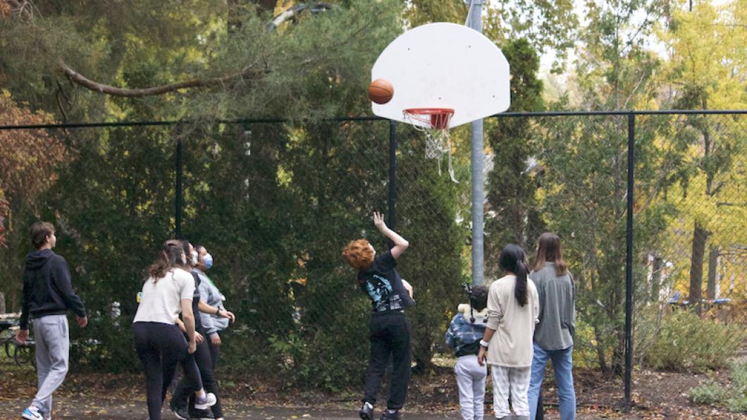 A number of children and teens on a basketball court as a teen with red hair throws the ball.