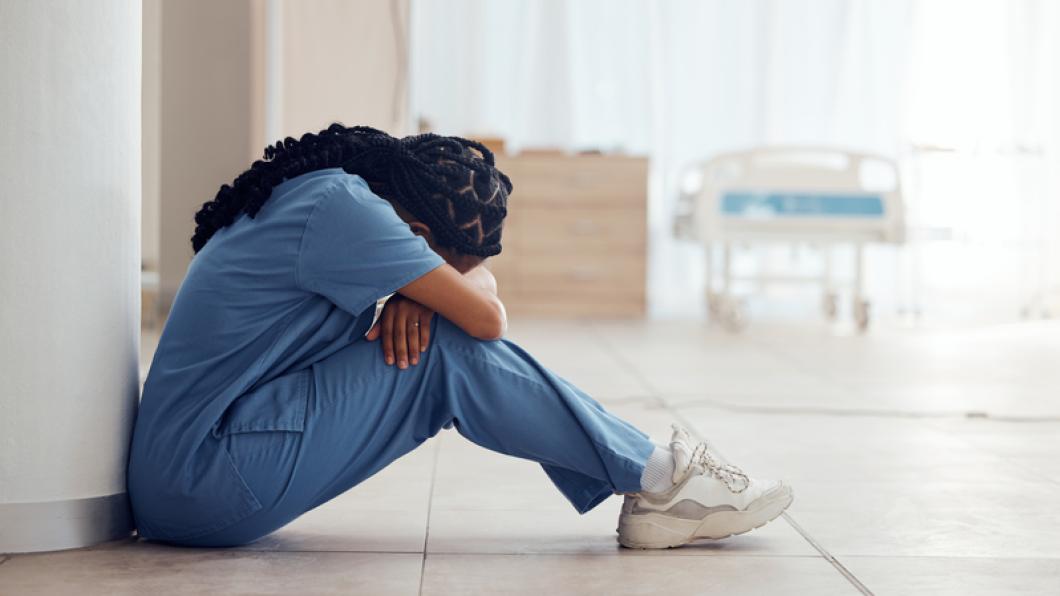 Woman with hair in braids and head on knees sitting on floor in scrubs
