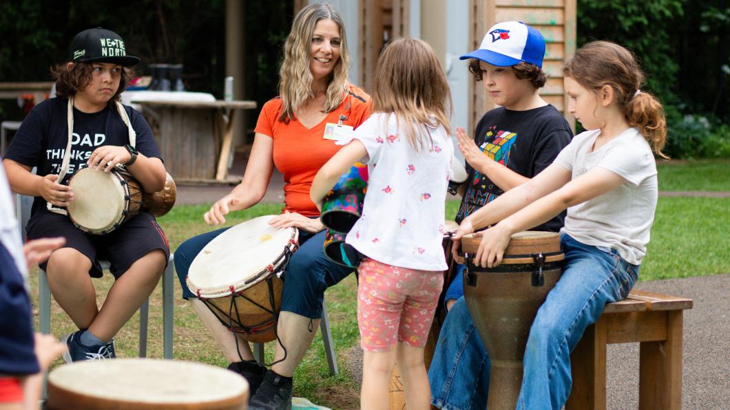Woman with long hair plays drum in the middle of a drum circle with children