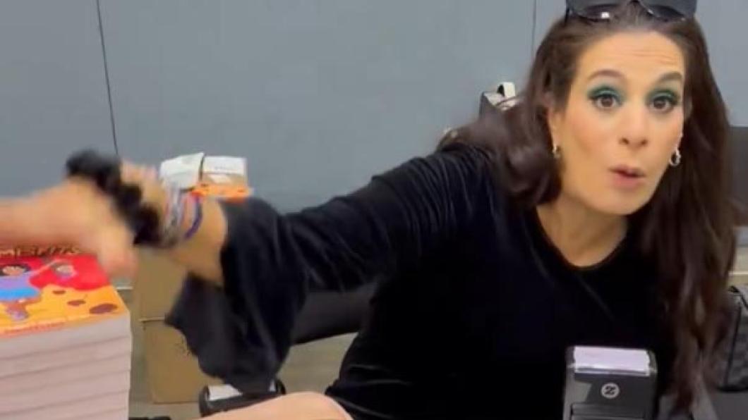 Woman with long dark hair sits at desk and puts hand on a pile of brightly coloured books