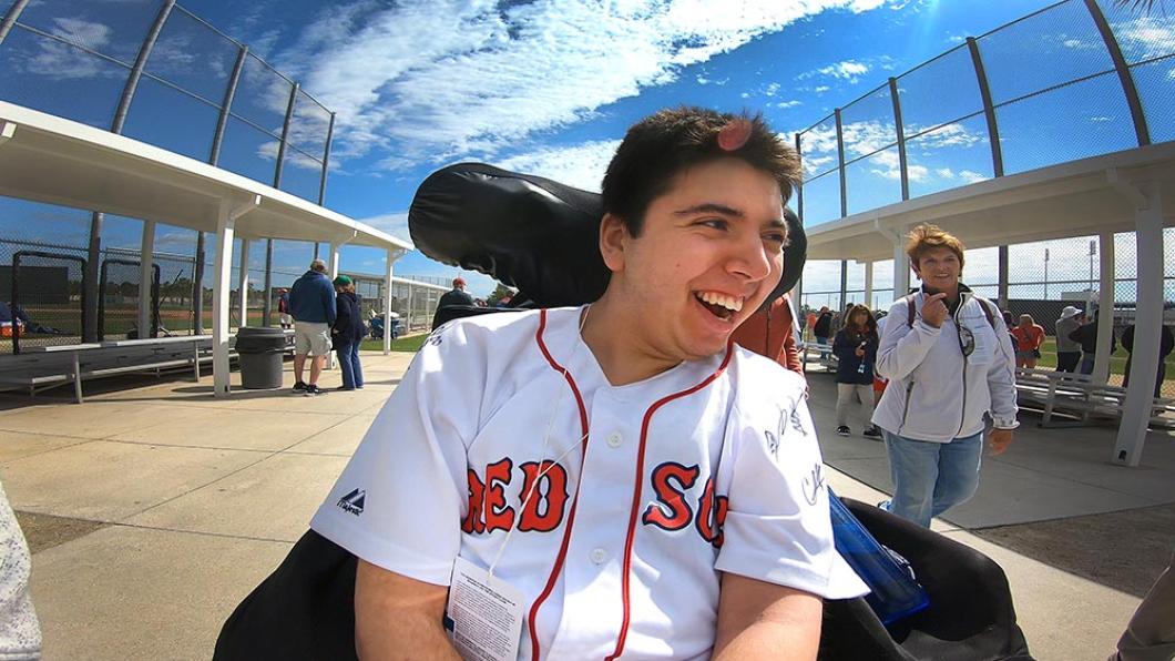 Young man with dark hair in Red Sox shirt smiles in wheelchair