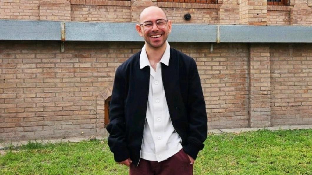 Man wearing glasses with white collared shirt and blue jacket smiles