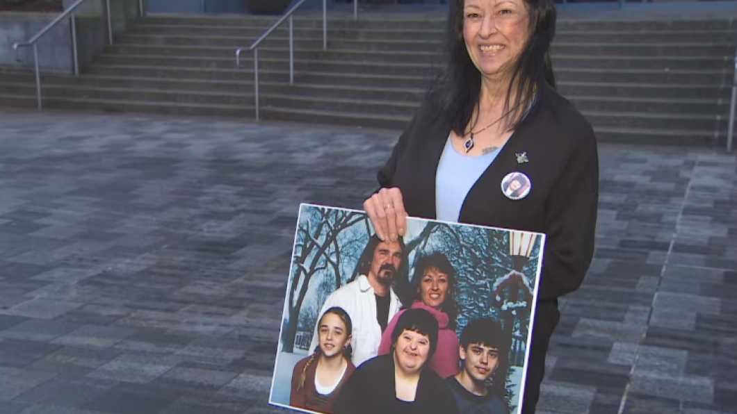 Woman with dark hair holds a large photo of a family