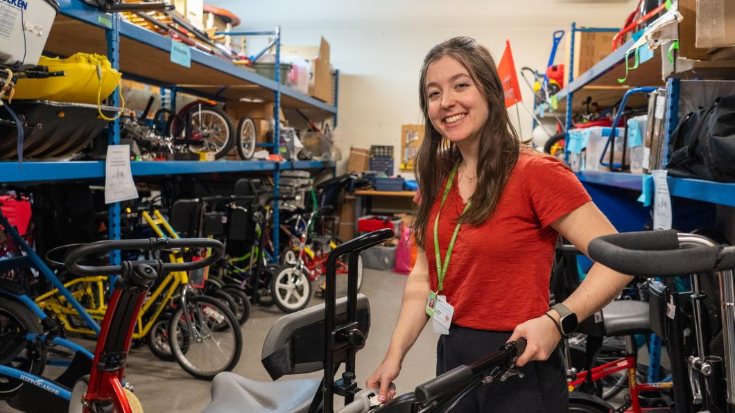 A young woman smiles and stands in a room of therapeutic recreation equipment.