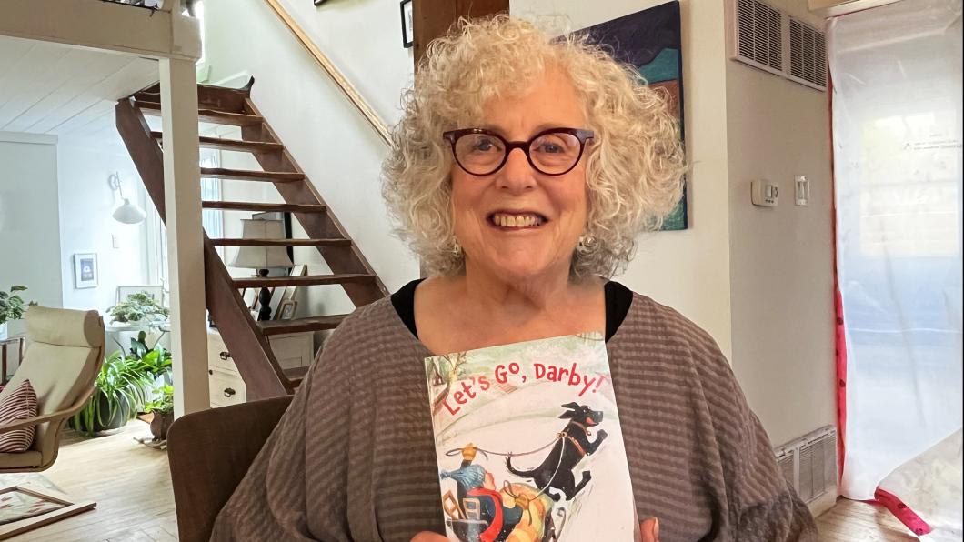 Woman with wavy white hair holds children's book