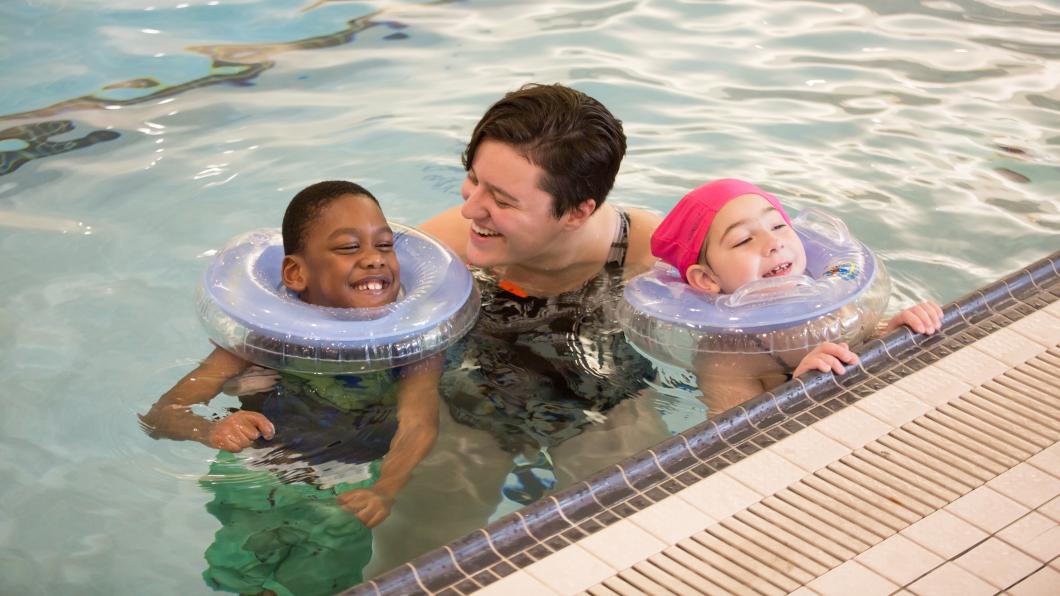 Two young kids at pool's edge with an adult