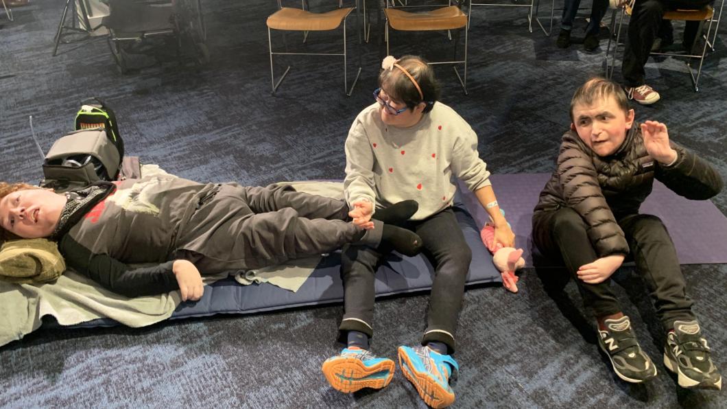 Young man lies on floor beside a woman and man with chairs lined behind them