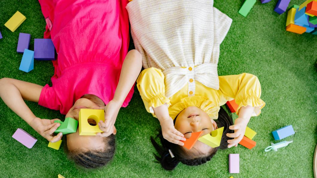 Two young children lie on the floor and play with blocks