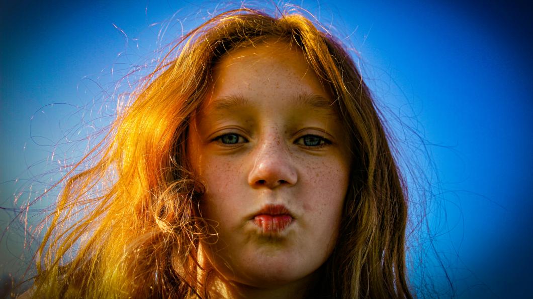 Girl with red hair purses lips on blue background