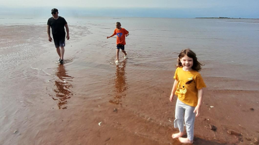 Girl in yellow shirt in water with red soil with man and boy behind her