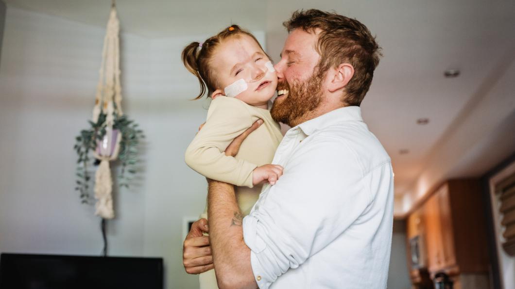 Man with beard hugs small girl with pony tails and nasal prongs