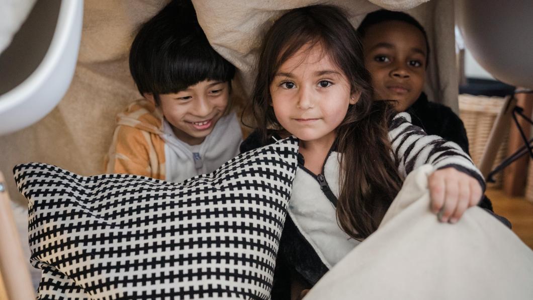 A girl and two boys play behind pillows