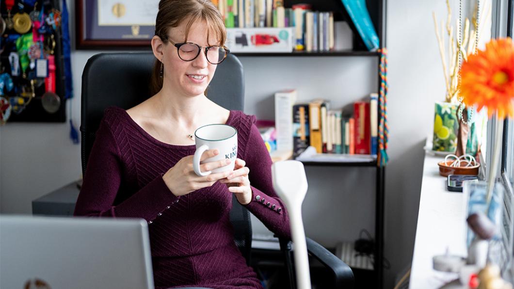 Woman with glasses and burgundy sweater holds mug in office