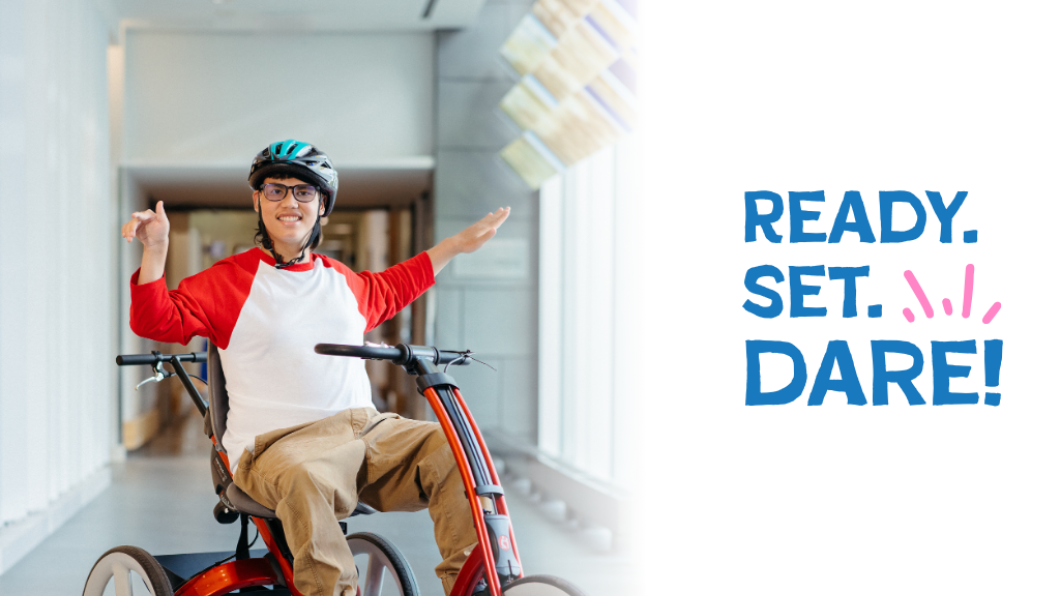 A young boy sitting on a bike, wearing a white shirt with red sleeves. The words "Ready. Set. Dare!" in a logo format are at the right side of the photo.