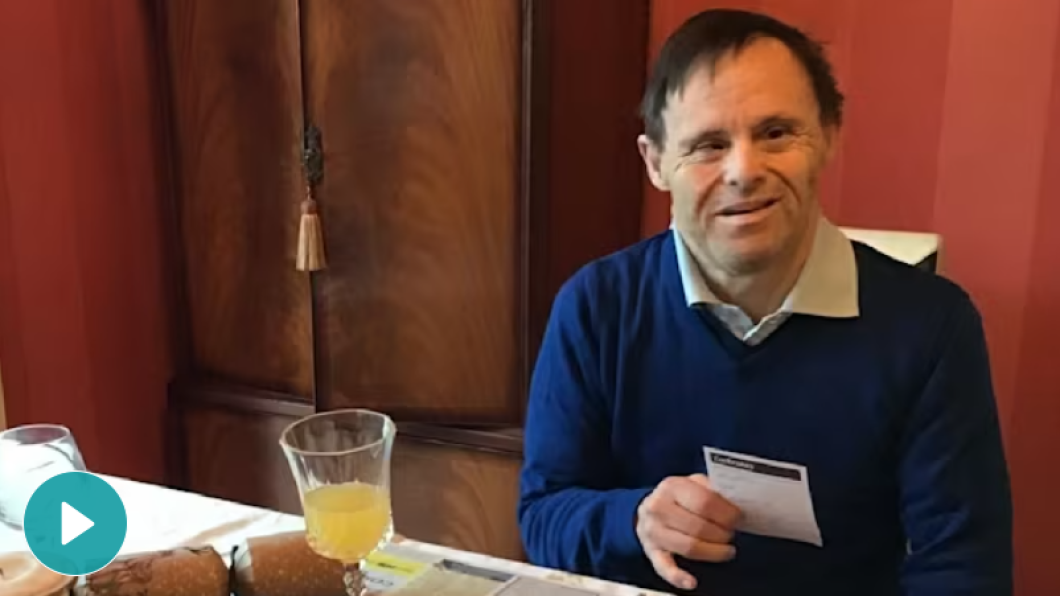 A man wearing a blue sweater sits at a table with a juice glass