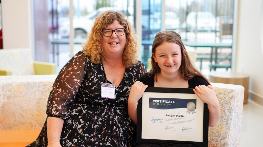 Dr. Carolyn Hunt and a child sitting beside each other on a couch. The child is holding up a framed certificate, and they are both smiling