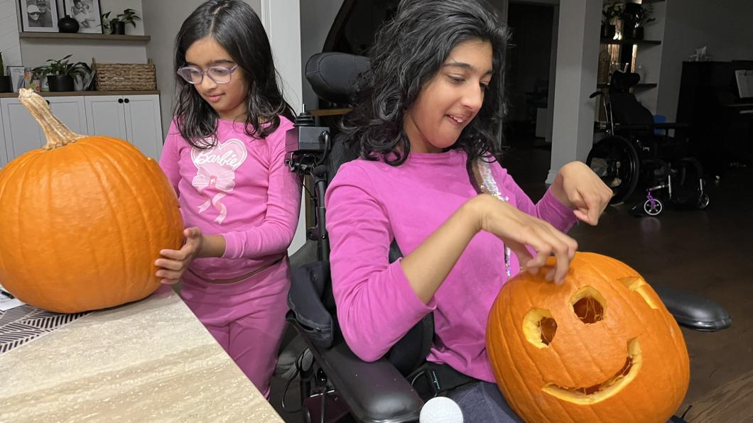 Two girls with pink shirts carve pumpkins