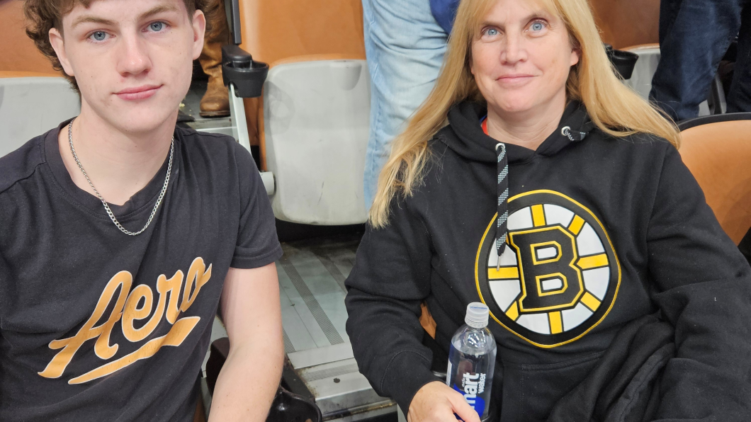 A teenage boy and his mom sit together at a hockey game.