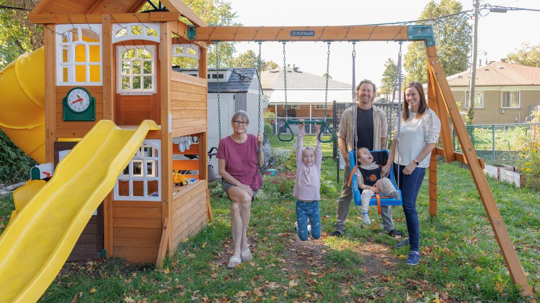 Young child wearing oxygen prongs in a swing beside a girl hanging from a bar with three adults in the background