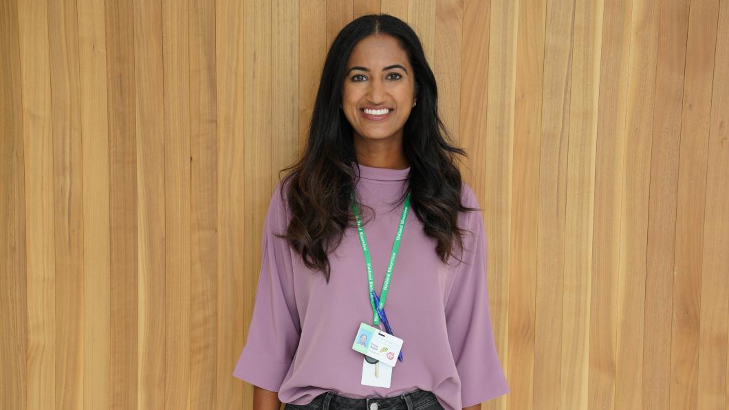 Woman with long dark hair and purple shirt wearing a green lanyard