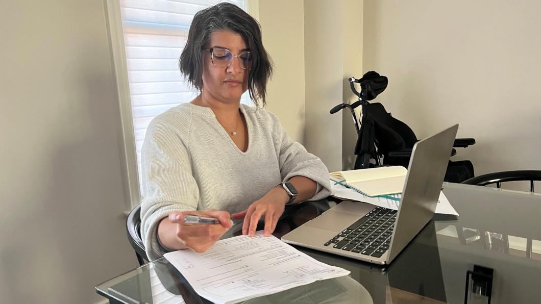Woman with dark hair in front of laptop and papers.