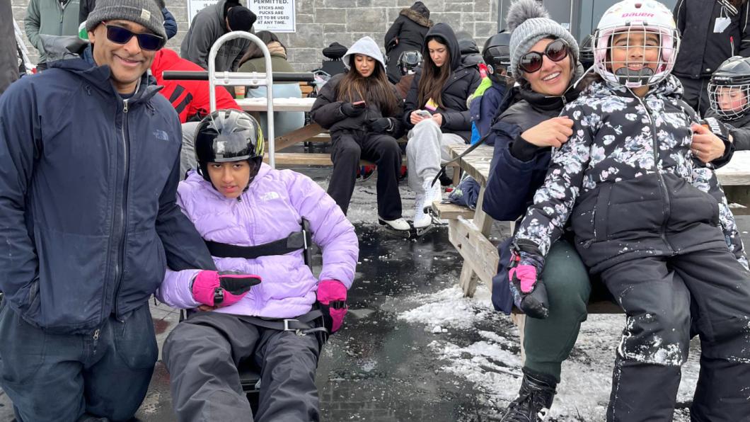 Teen in purple jacket on sledge holds hand of man beside girl in skates sitting on woman's lap