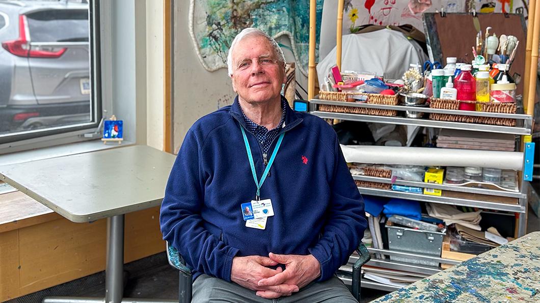 A man sits in an art therapy room with his hands in his lap. 