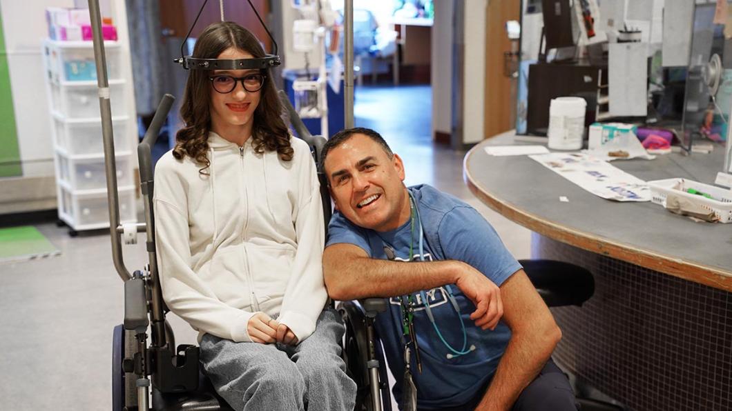 An adult with a teenager who is sitting on a wheelchair