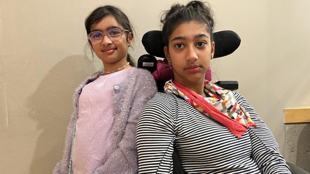 Teen with dark hair and red scarf in wheelchair beside girl with dark hair and pink shirt