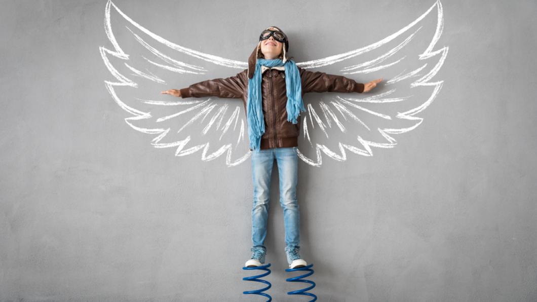 Boy stands on springs with arms spread on wall image of wings